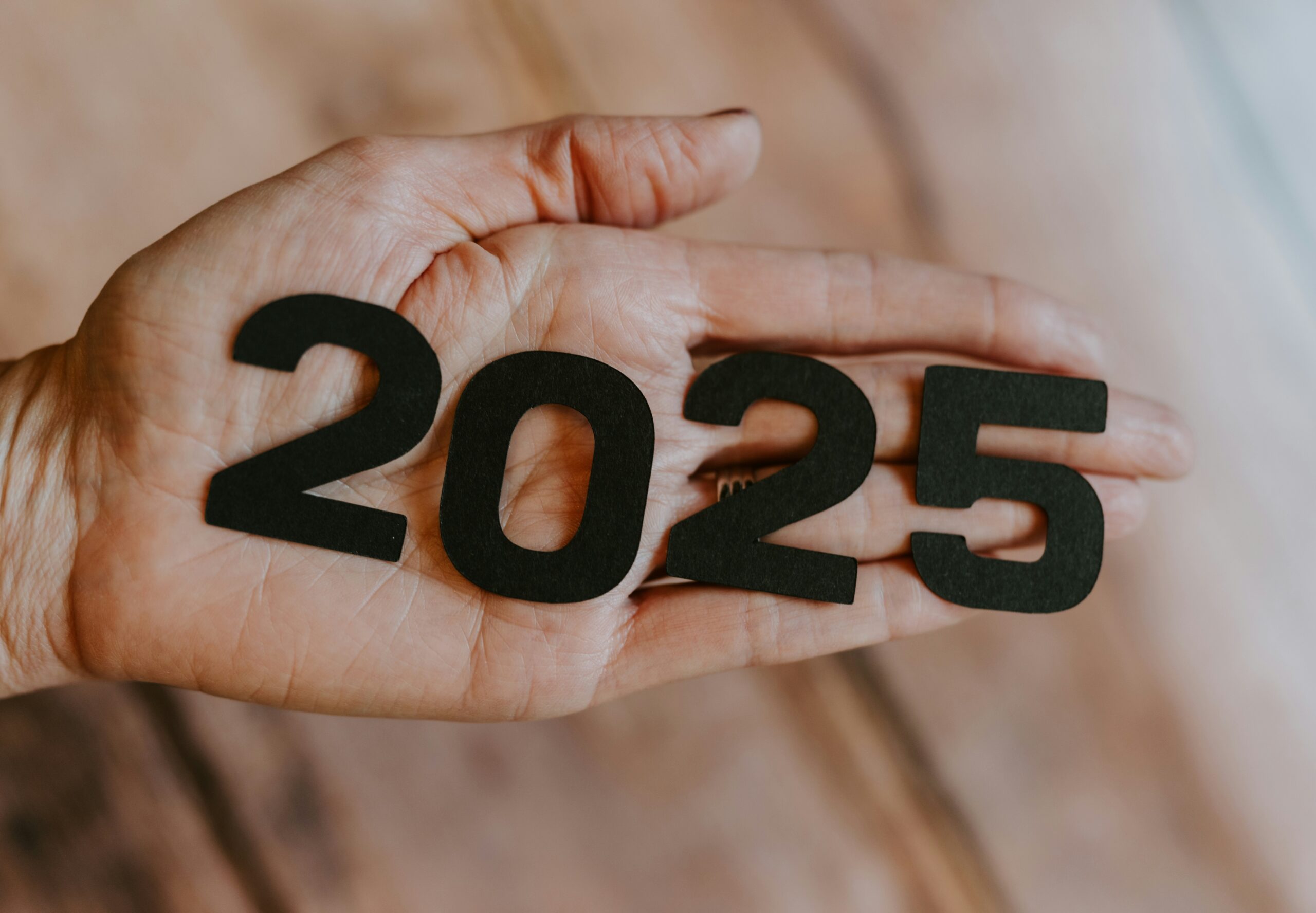 a mao de uma pessoa segurando o numero 2025 recortado em papel preto.
